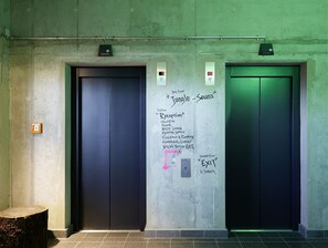 Dos puertas de ascensor con grafitis y anotaciones escritas a mano que señalan indicaciones a diferentes lugares dentro de un edificio.