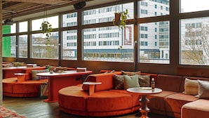 A modern interior with a large window, orange seating, and a patterned rug. - 25hours Hotel Bikini Berlin (Berlin)
