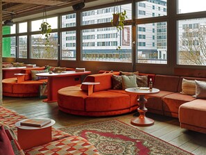 A modern interior with a large window, orange seating, and a patterned rug. - 25hours Hotel Bikini Berlin (Berlin)