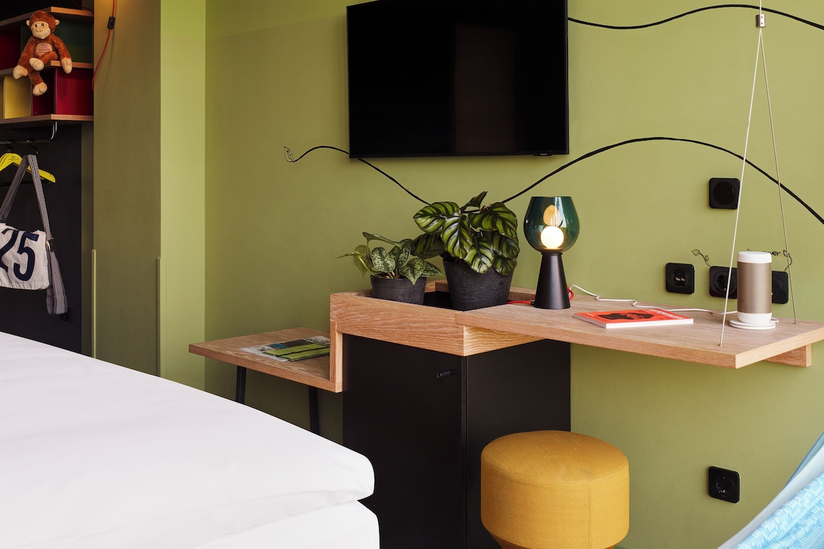 Un dormitorio con una cama, un escritorio con lámpara, un televisor y una planta en maceta.