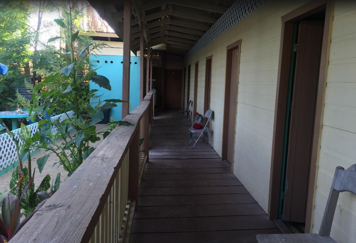 A covered wooden corridor with a wooden railing, a folding chair, and a door on the right.