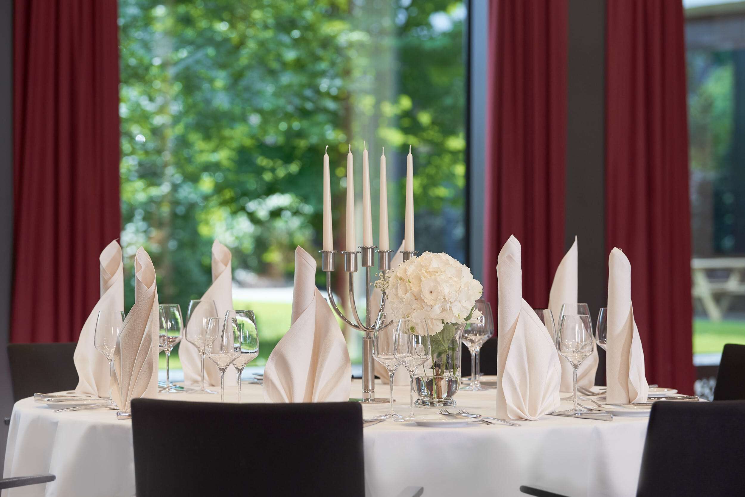 A table set for a meal with white napkins, clear glassware, and a candle holder with white flowers.