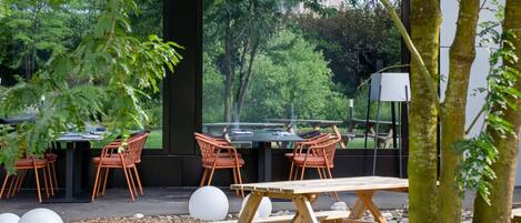 An outdoor dining area with tables and chairs, surrounded by trees and a view of a building.