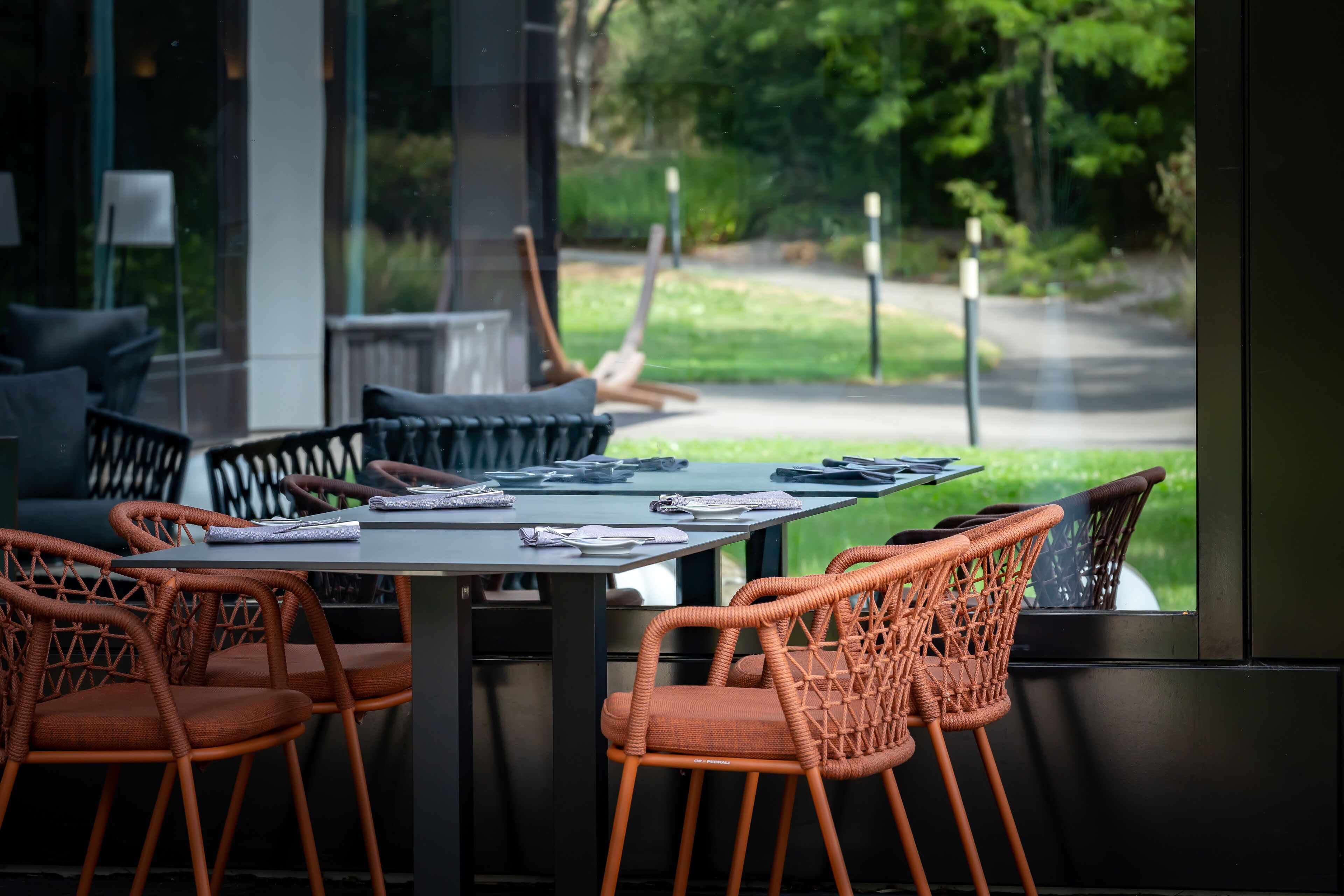 Mesa lista para comer con sillas de mimbre, vista a un paisaje verde a través de una ventana y un diseño interior moderno.
