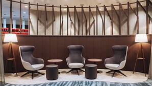 Un vestíbulo moderno con tres sillones tapizados, dos mesitas redondas y lámparas de pie.