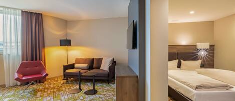 A hotel room with a bed, a sofa, a red chair, a small table, and a TV.