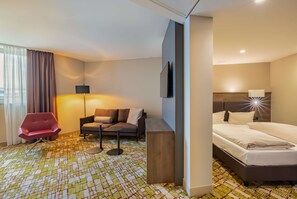 A hotel room with a bed, a sofa, a red chair, a small table, and a TV. - Dorint Airport-Hotel Zürich (Opfikon)