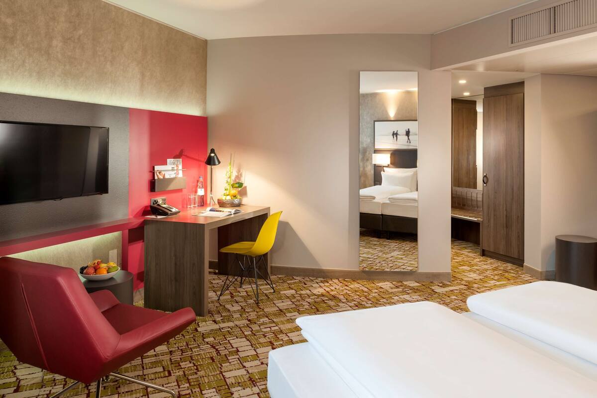 A hotel room with a TV, desk, chair, bed, and a mirror.