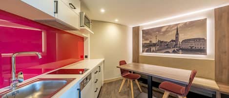 A modern kitchen with a red accent wall, stainless steel sink, and a dining area with a wooden table and red chairs.