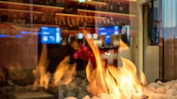 A fire feature with logs and a glass barrier, a seating area, and a bar with screens in the background.