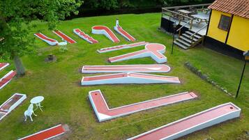 A large outdoor area with multiple mini golf holes and a yellow building with a red roof.