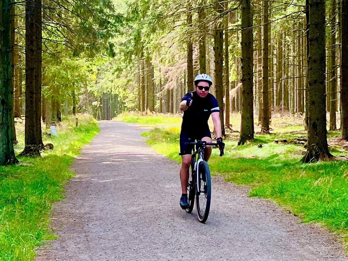 A cyclist on a paved path surrounded by trees.