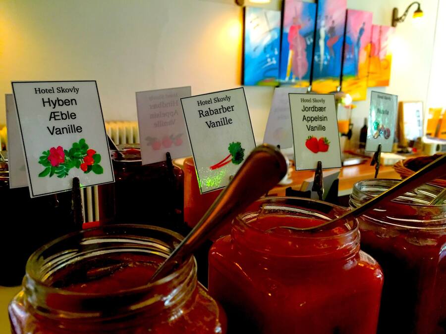 Botes de mermelada con etiquetas que indican sabores como 'Hyben Vanille' y 'Rabarber Vanille' en el Hotel Skovly.