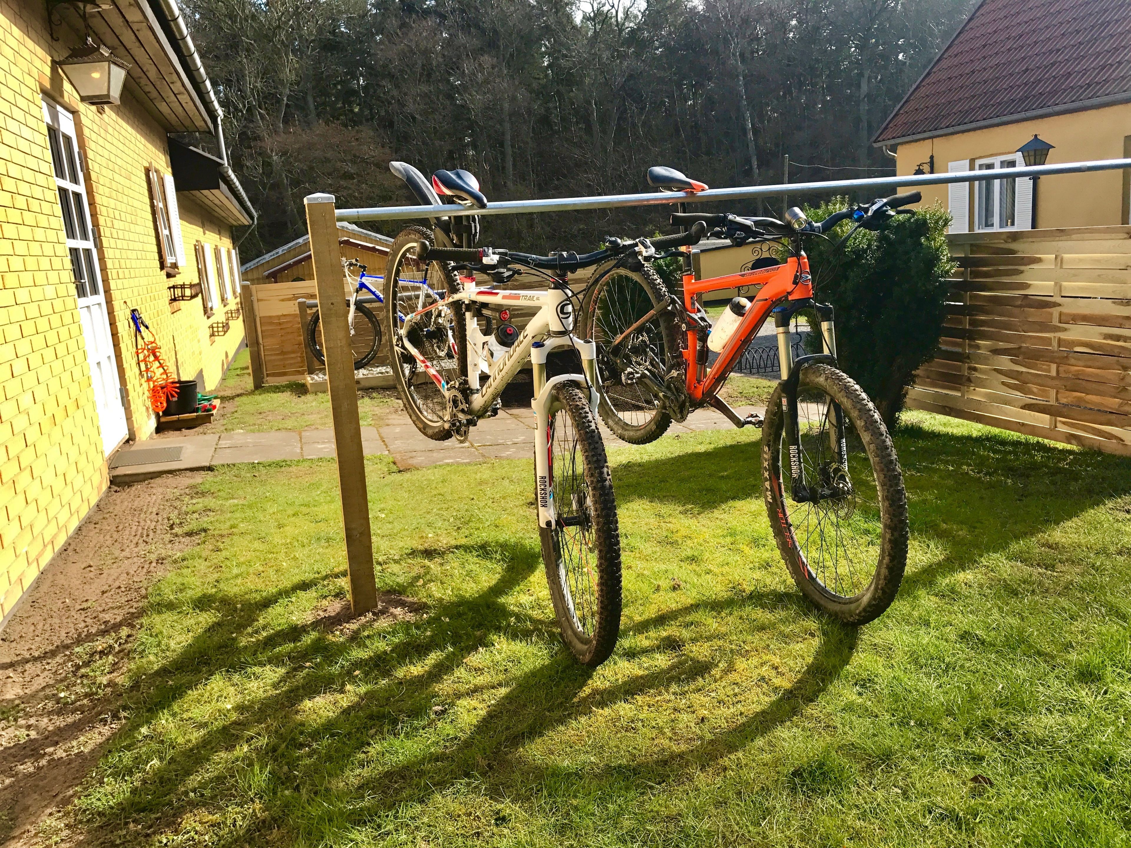 A bicycle rack with two bicycles, a brick house, and a wooden fence.