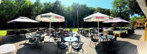 An outdoor patio area with round tables and chairs, covered by umbrellas with 'Benediktiner' and 'Weissbier' branding. - Hotel Skovly (Ronne)
