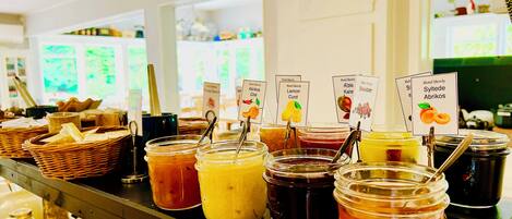 Mostrador tipo buffet con diversas opciones de comida y bebida, incluyendo frascos de salsas y condimentos, y etiquetas que indican los nombres de los platos.