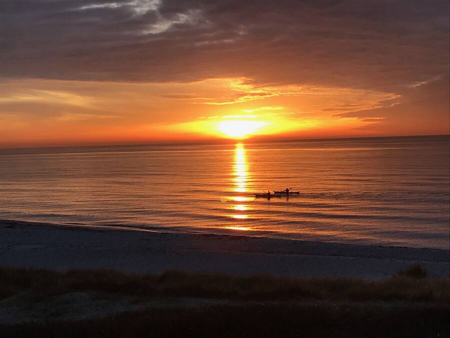 A sunset over a calm sea with a beach in the foreground.
