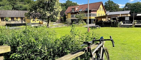 A bicycle parked near a wooden fence with a grassy area and a yellow building in the background.