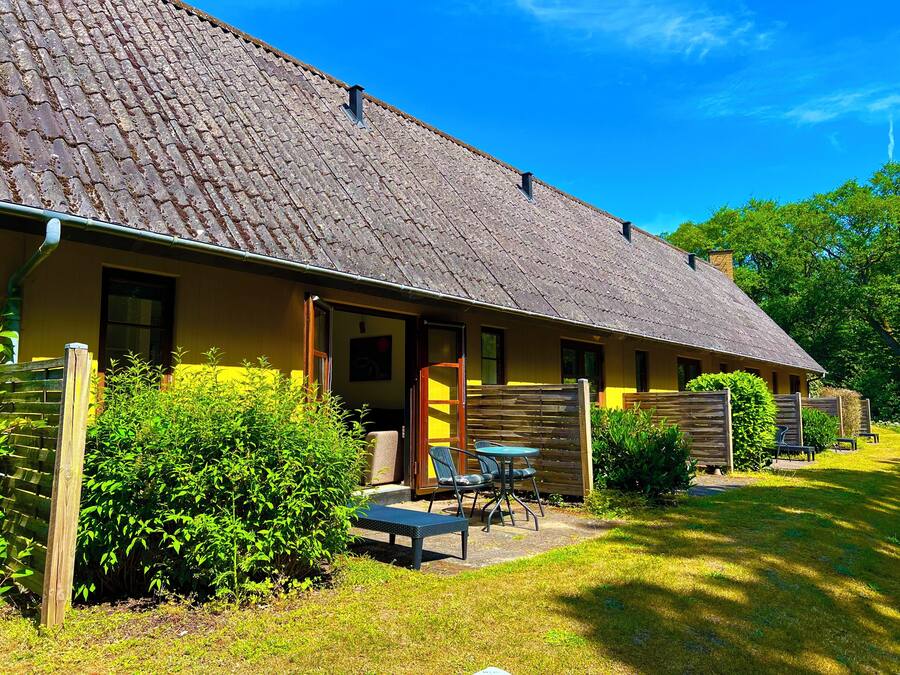 A rustic building with a tiled roof, a wooden fence, and a small patio area with a table and chairs.