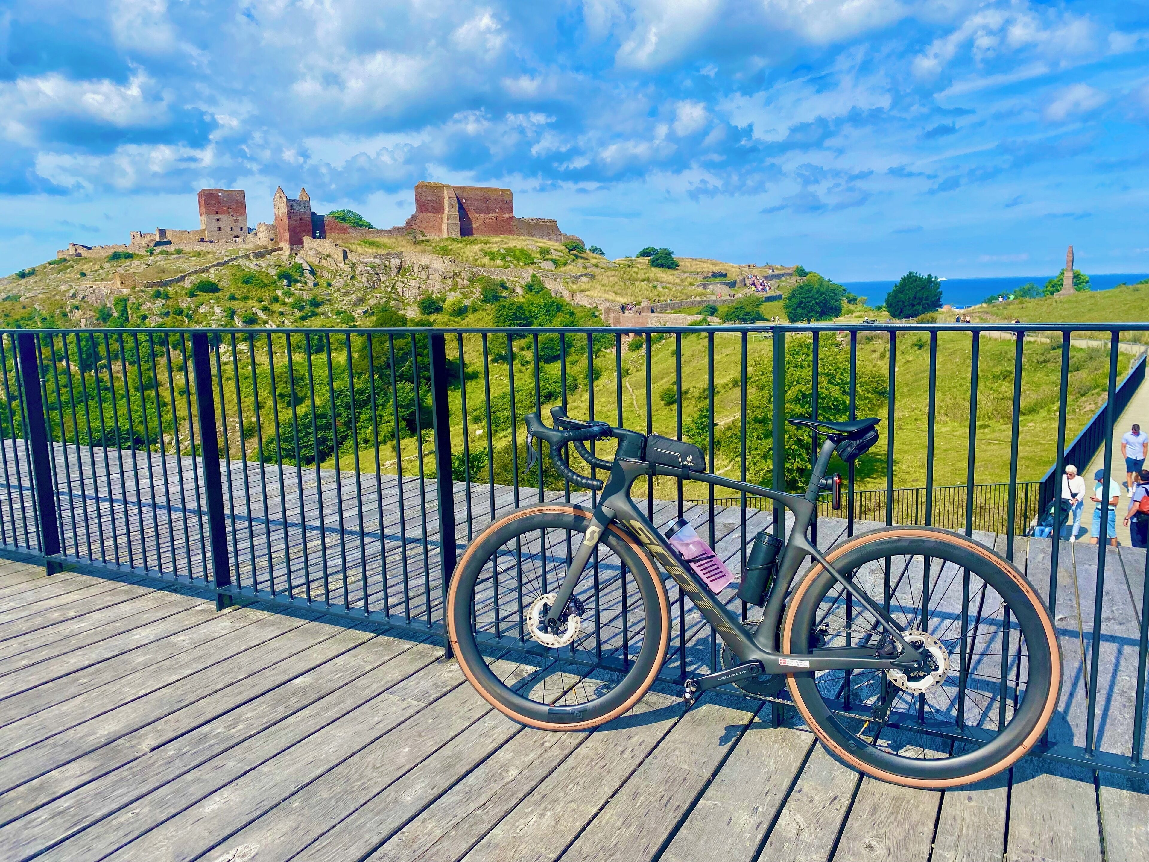 Una bicicleta estacionada en una terraza de madera, con una vista de un castillo histórico al fondo.