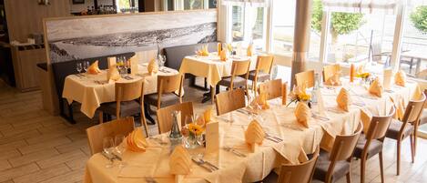A restaurant with multiple tables set for dining, featuring yellow tablecloths and wooden chairs.