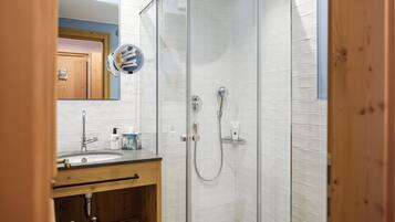 A modern bathroom with a glass shower enclosure, a wooden vanity, and a white tiled wall.