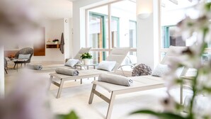 A modern spa room with lounge chairs, a small table with a plant, and a chair with a towel. - Landhaus Am Stein Tegernsee (Bad Wiessee)