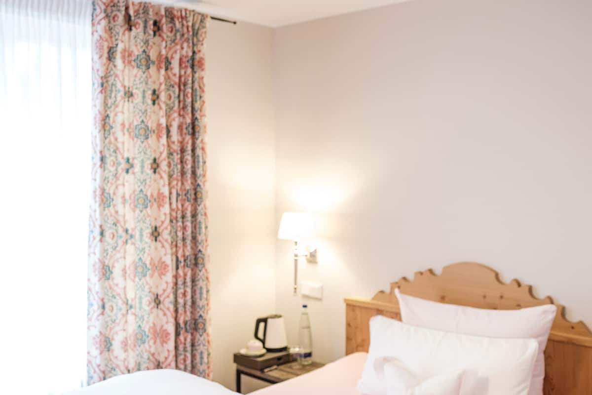 Una cama bien hecha con sábanas blancas, cabecera de madera y mesita de noche con lámpara y botella.