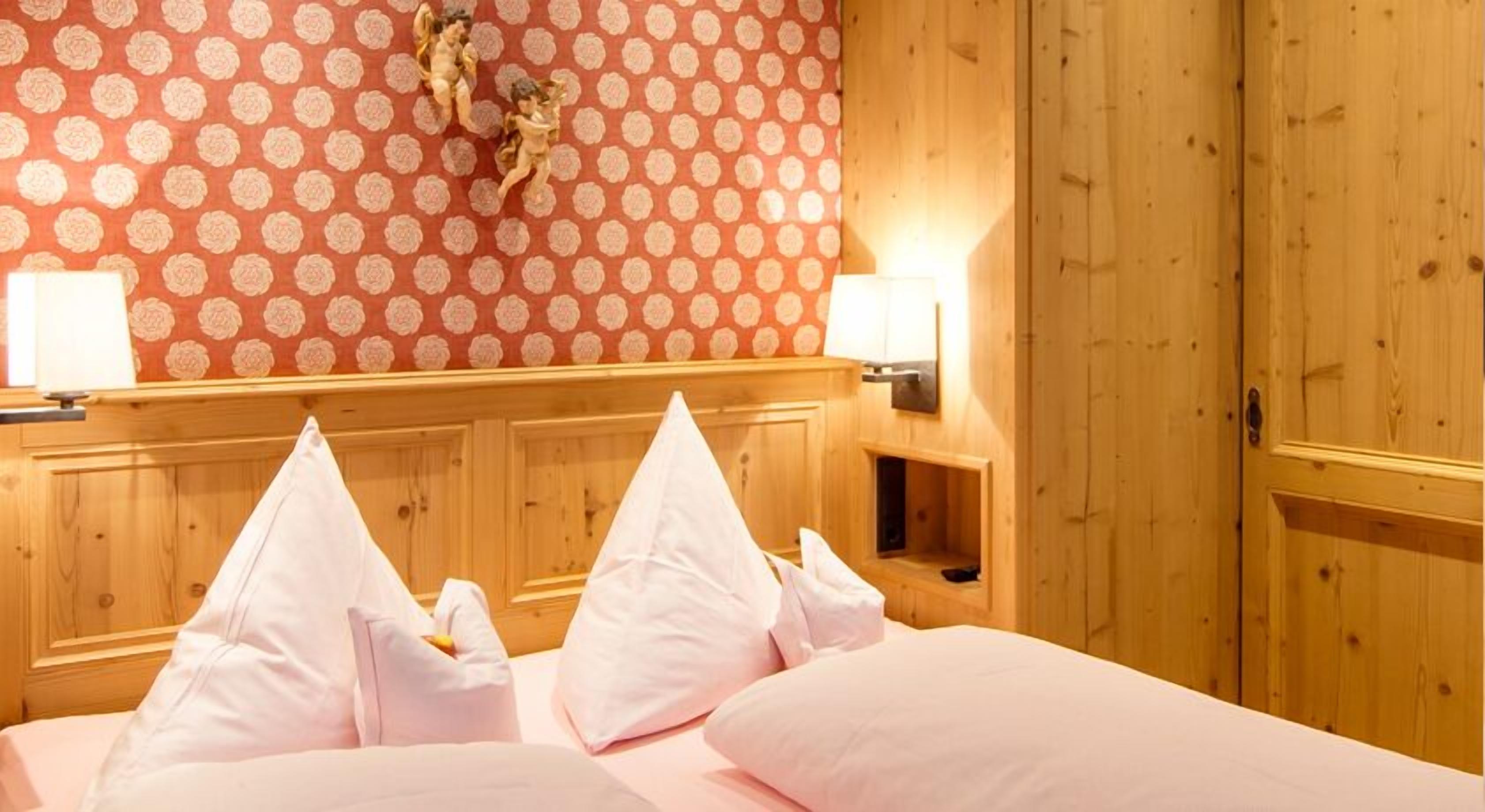 Quarto de hotel com cabeceira de madeira, parede estampada com flores e cama com almofadas brancas.