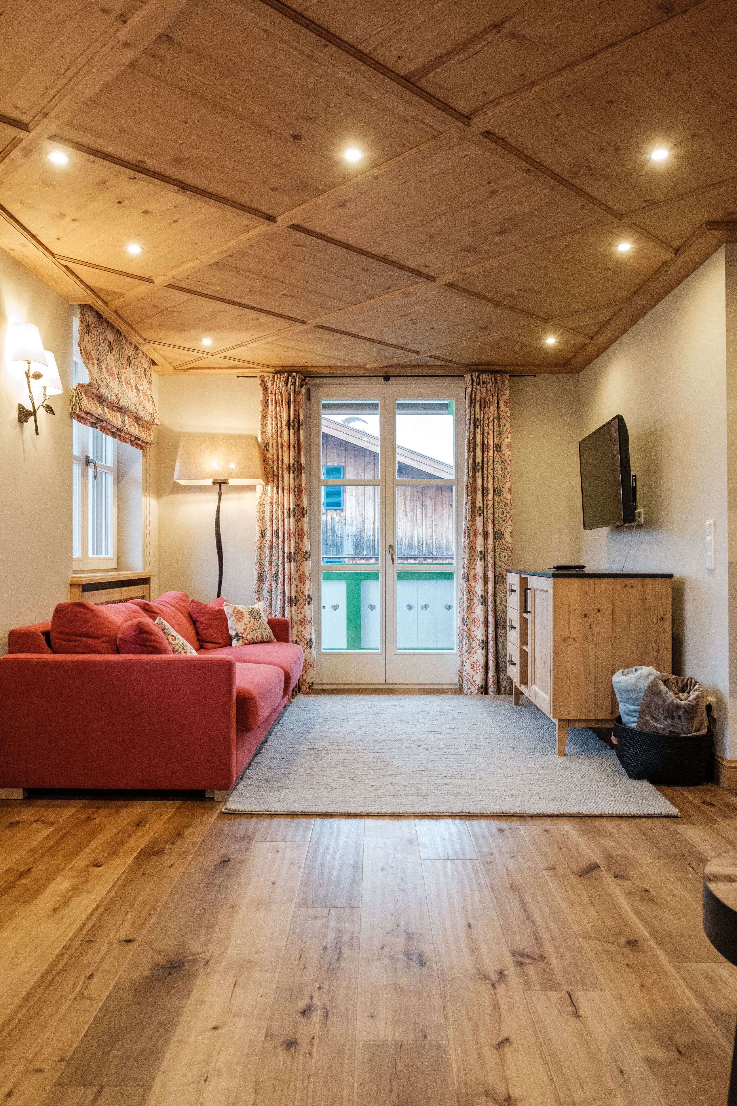 A cozy living room with a wooden ceiling, a red sofa, a wooden cabinet, and a television.