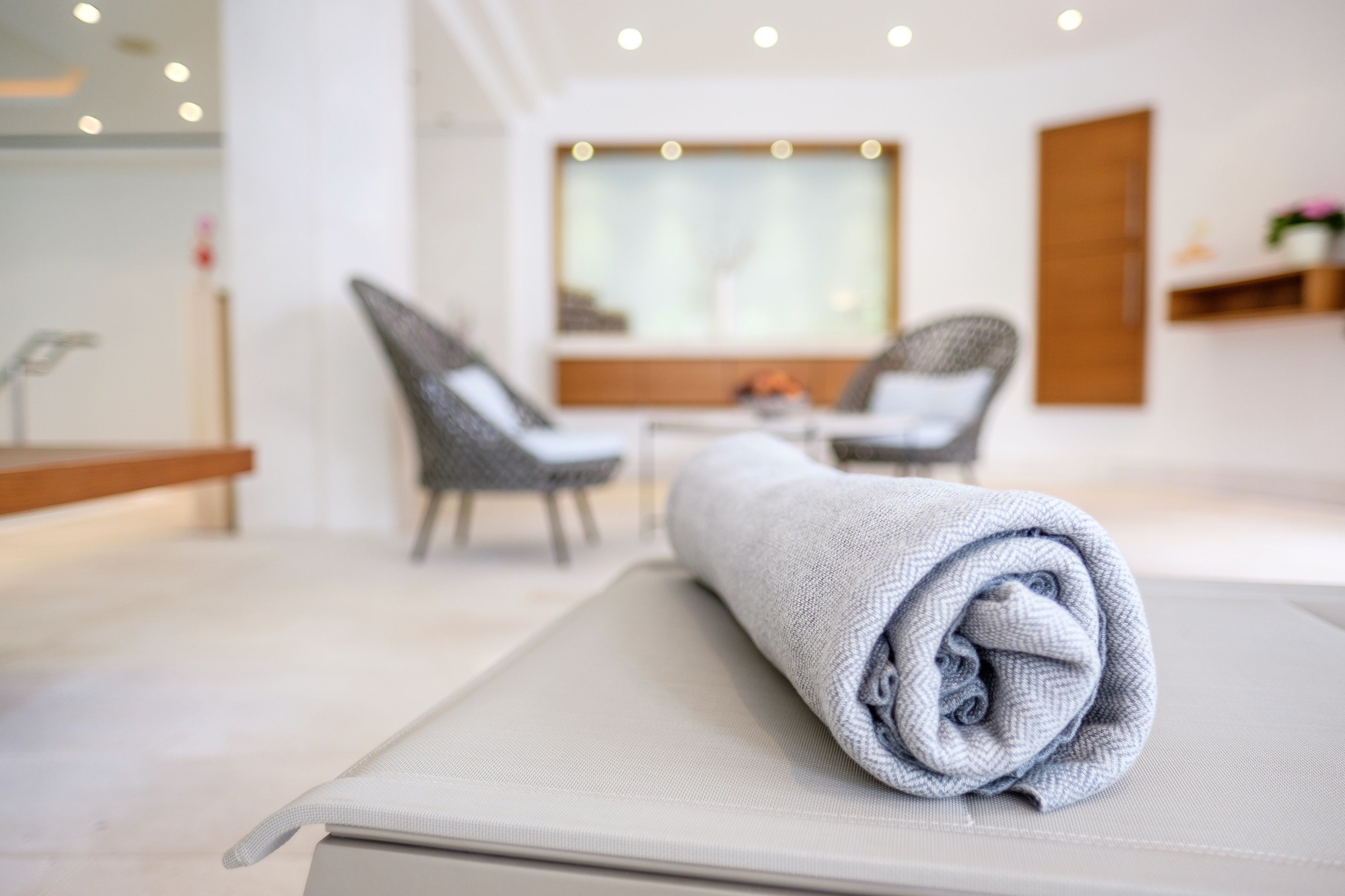 Una habitación ordenada con una toalla enrollada sobre un tapete, una silla y una mesa con un florero.