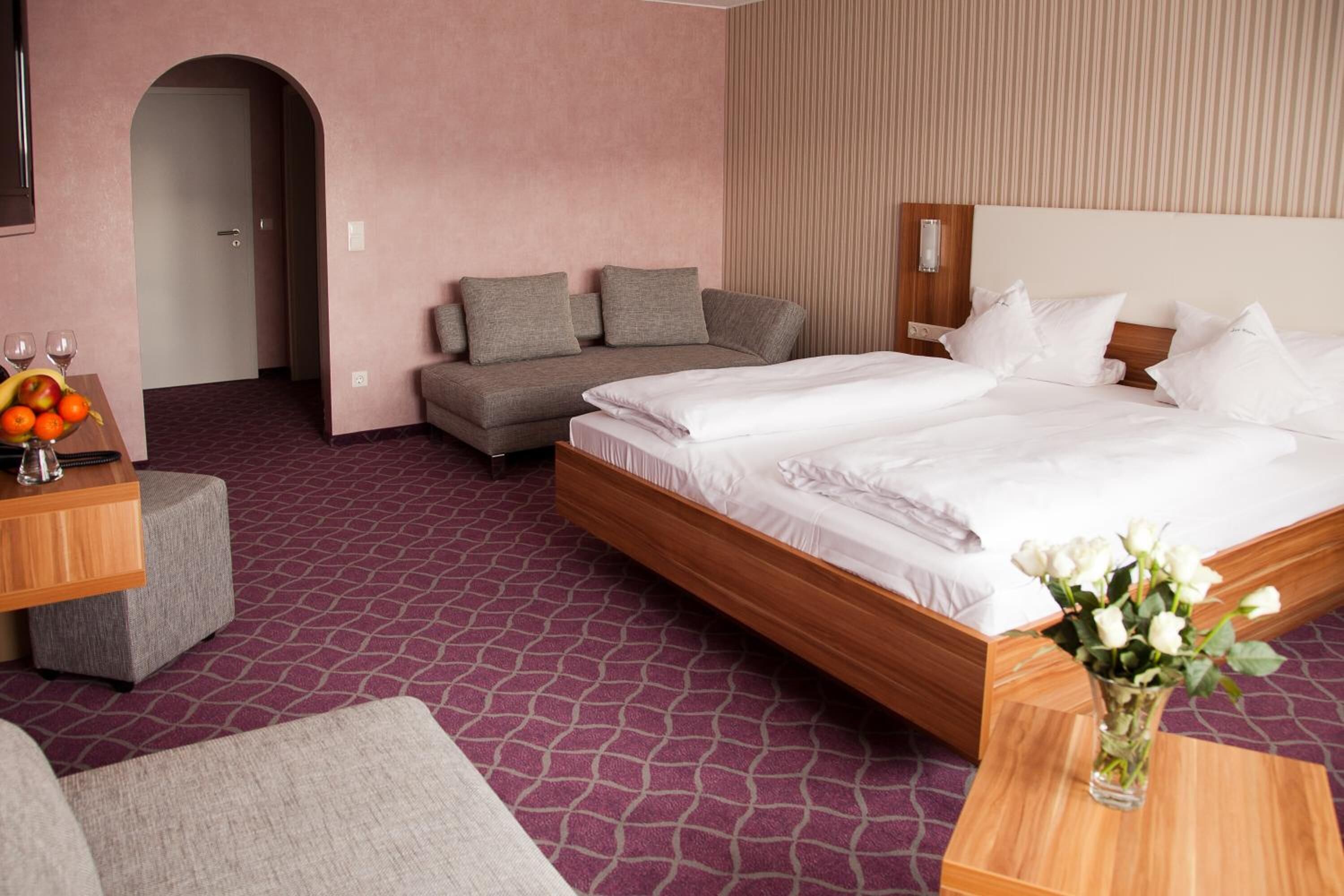 A hotel room with a large bed, a sofa, a small table with a vase of flowers, and a fruit bowl.