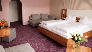 A hotel room with a large bed, a sofa, a small table with a vase of flowers, and a fruit bowl.