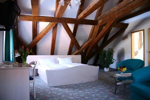 Un dormitorio con techo de madera, una cama, un escritorio con teléfono, una silla, una mesita con fruta y una planta en maceta.