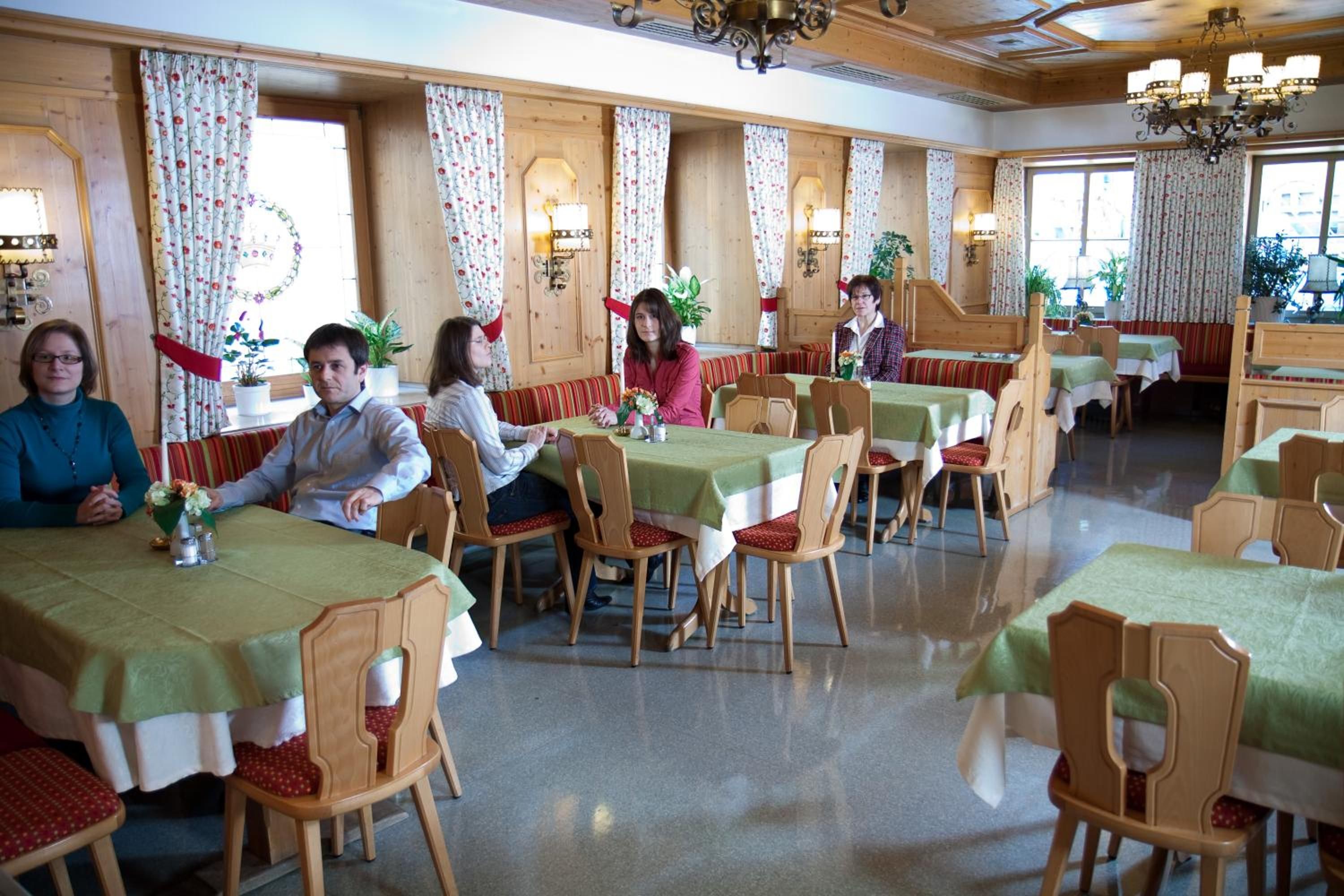 A dining area with wooden tables and chairs, floral curtains, and a chandelier.