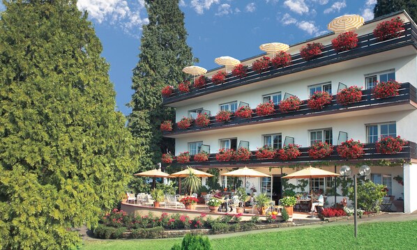 A multi-story hotel with outdoor seating and flower boxes on balconies. - Hotel Behringers Traube (Badenweiler)