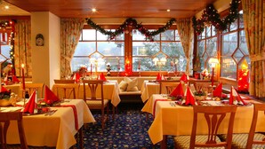 A warmly decorated dining area with tables set for a meal, featuring festive decorations and a view of the outdoors. - Hotel Behringers Traube (Badenweiler)