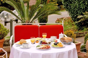 A table set outdoors with a variety of breakfast items including fruits, pastries, and beverages. - Hotel Behringers Traube (Badenweiler)