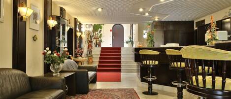 Un hall d’hôtel avec un canapé en cuir, un tapis à motifs, un escalier et des tabourets de bar.