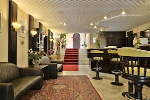 Um hall de hotel com sofá de couro, tapete estampado, escada e banquetas de bar.