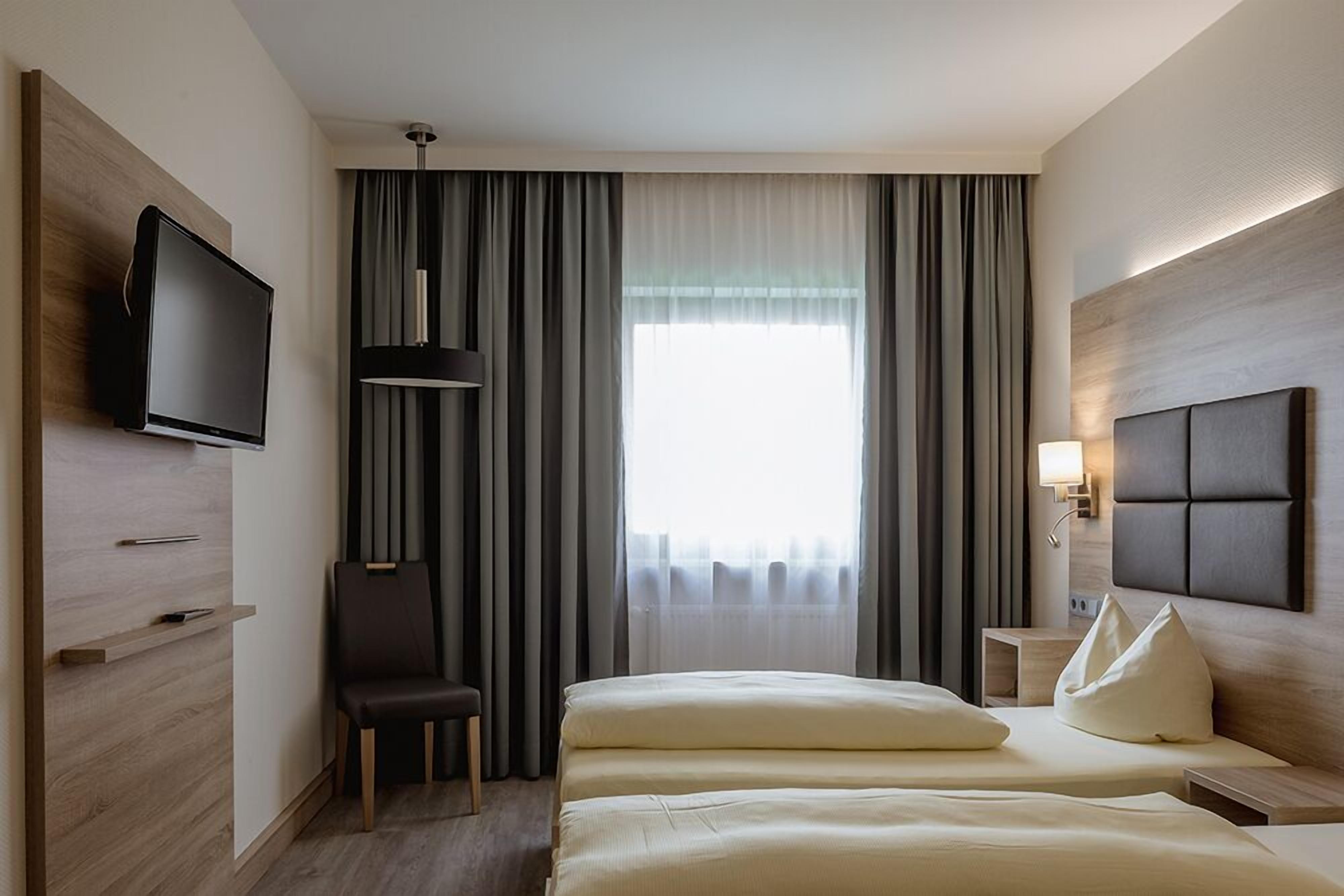 A hotel room with a bed, a TV, a chair, and a window with curtains.