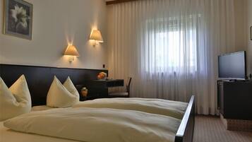 A hotel room with a bed, two bedside lamps, a desk with a chair, a television, and a window with curtains.