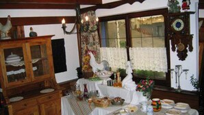 Un comedor con una mesa dispuesta para comer, rodeado de armarios de madera y una ventana con cortinas de encaje.