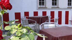 Un área de estar al aire libre con sillas y mesas de metal, pared a rayas rojas y blancas, y rosas rojas en primer plano.