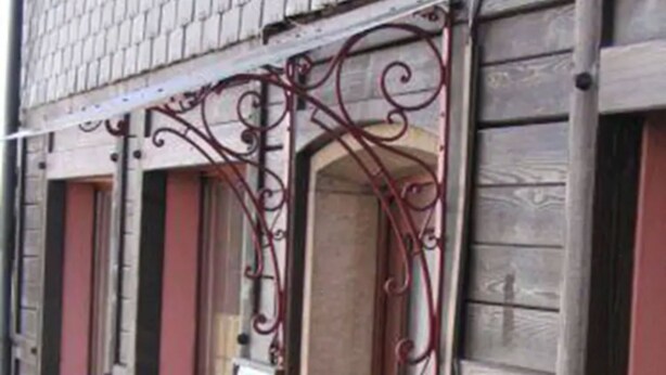 Un edificio con fachada de madera, varias ventanas con contraventanas y barandillas decorativas de hierro forjado.