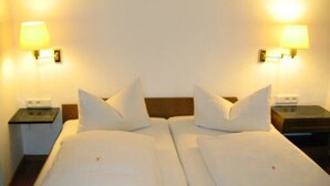 Una cama doble con sábanas blancas y dos mesitas de noche, cada una con una lámpara.