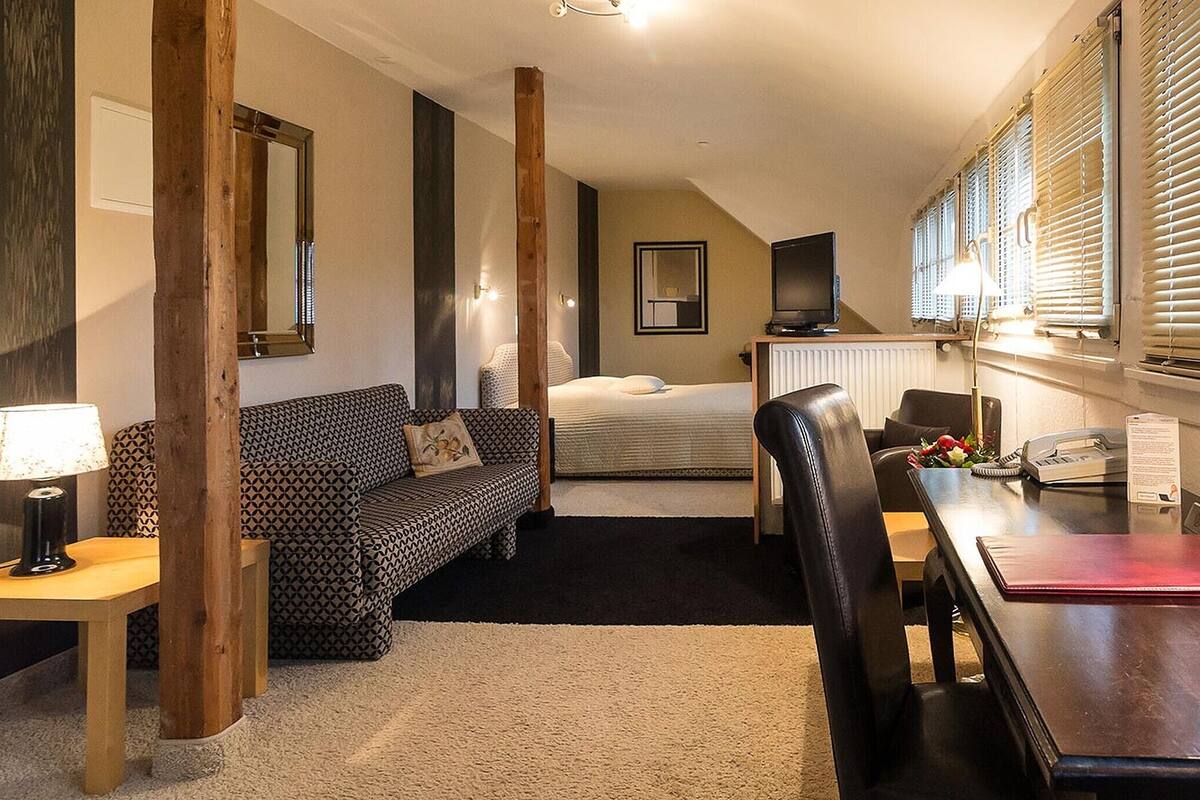 A cozy room with a bed, a sofa, a dining table, and a lamp.