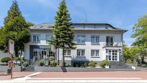 A two-story building with a modern architectural style, featuring a prominent entrance with a glass door and a staircase leading to the main entrance. - Thermen Hotel Bad Soden am Taunus (Bad Soden am Taunus)