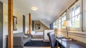 A bedroom with a bed, a desk with a lamp, a chair, a sofa, and a window with a view. - Thermen Hotel Bad Soden am Taunus (Bad Soden am Taunus)
