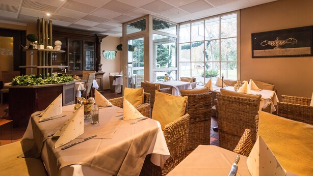 A restaurant with wicker furniture, large windows, and a view of greenery outside. - Thermen Hotel Bad Soden am Taunus (Bad Soden am Taunus)